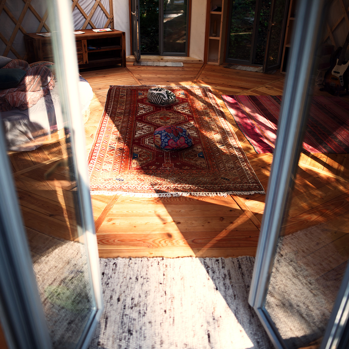 Gemütlicher Innenraum einer Jurte mit Teppich, Kissen und Holzboden – Wohnen in der Jurte erleben