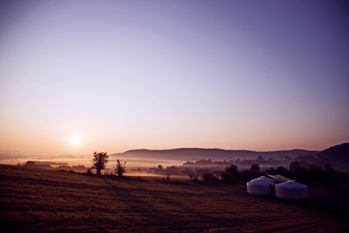 Jurten auf einer Wiese im Sonnenaufgang mit Blick auf Hügel und Nebel