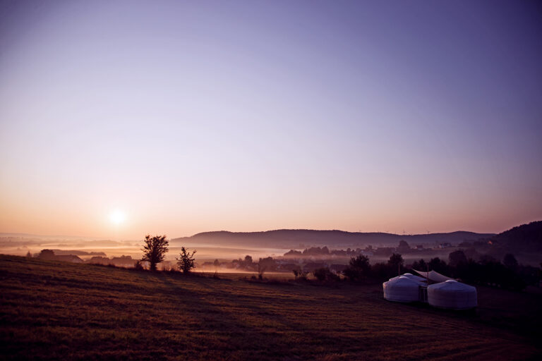 Sonnenaufgang über Jurtenlandschaft Jurten auf einer Wiese im Sonnenaufgang mit Blick auf Hügel und Nebel