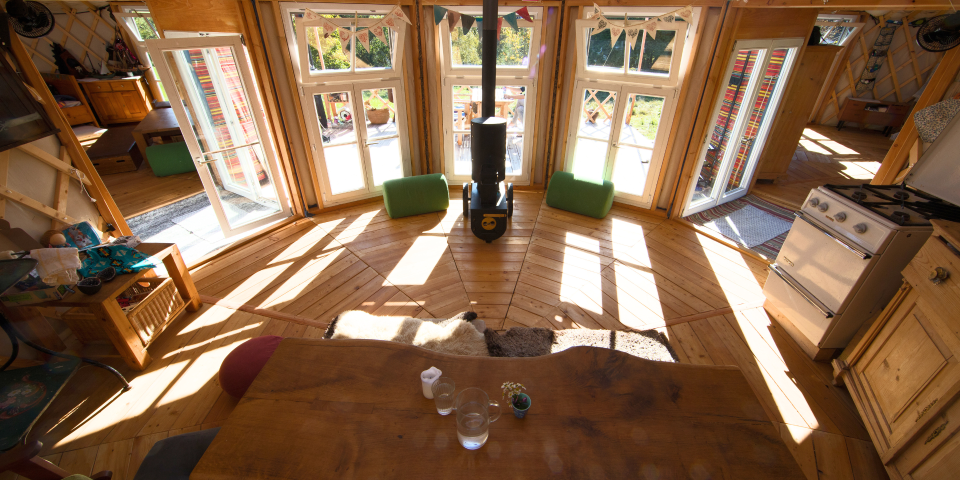 Blick ins Innere einer Jurte mit Holzboden, Dachkranz und Sonnenlicht durch die Fenster