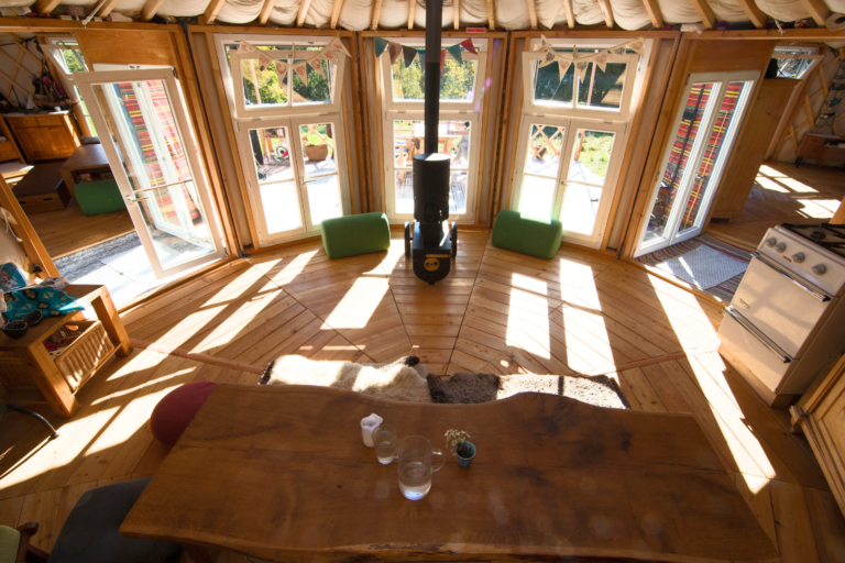 Blick ins Innere einer Jurte mit Holzboden, Dachkranz und Sonnenlicht durch die Fenster